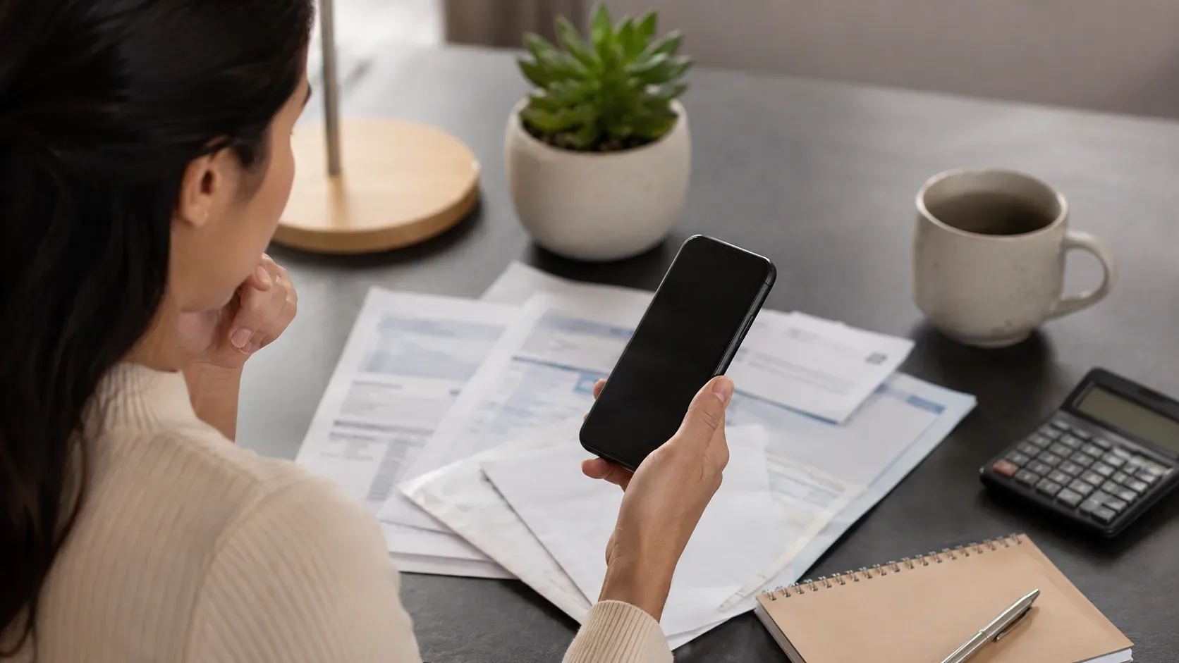 Pessoa consulta informações sobre uma dívida antiga em um celular, com documentos financeiros sobre a mesa