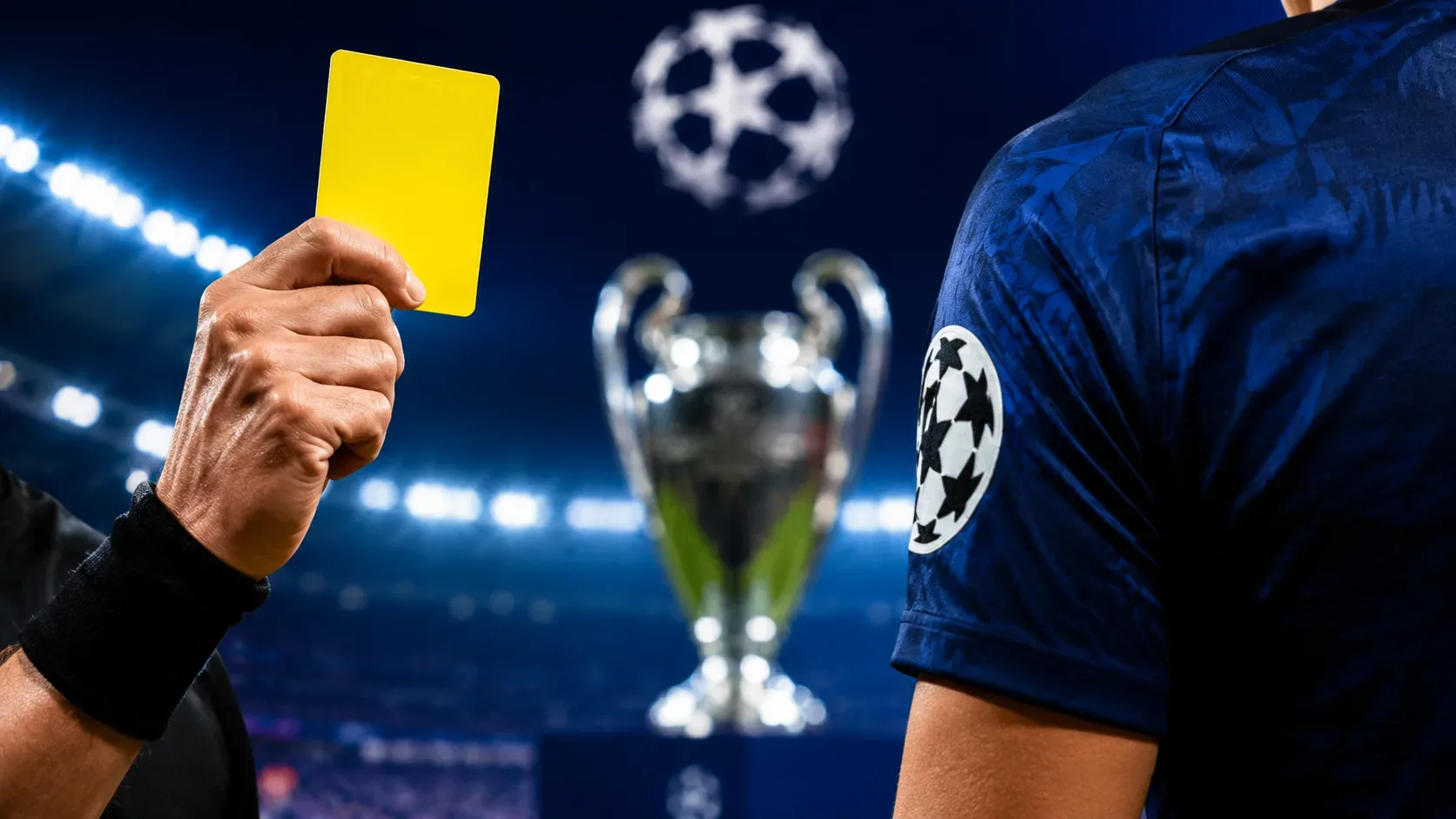 Árbitro ergue cartão amarelo diante de jogador de uniforme azul, com troféu e estádio iluminado desfocados ao fundo.