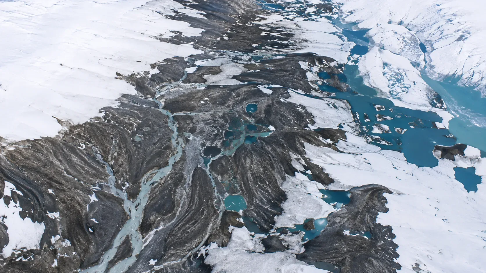 Imagem de satélite da Barnes Ice Cap em 12 de julho de 2026, com gelo cinza exposto, poças azuis e canais de água de degelo.