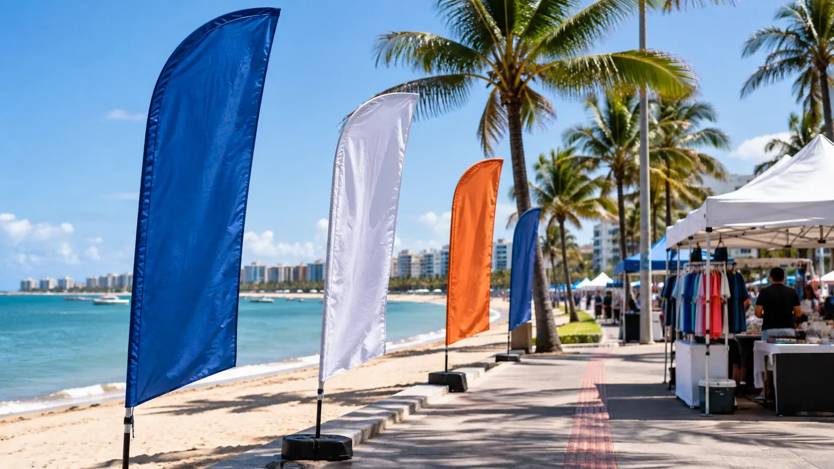 Orla tropical de Maceió com calçadão, palmeiras, tendas comerciais e wind banners coloridos ao longo da faixa de praia.