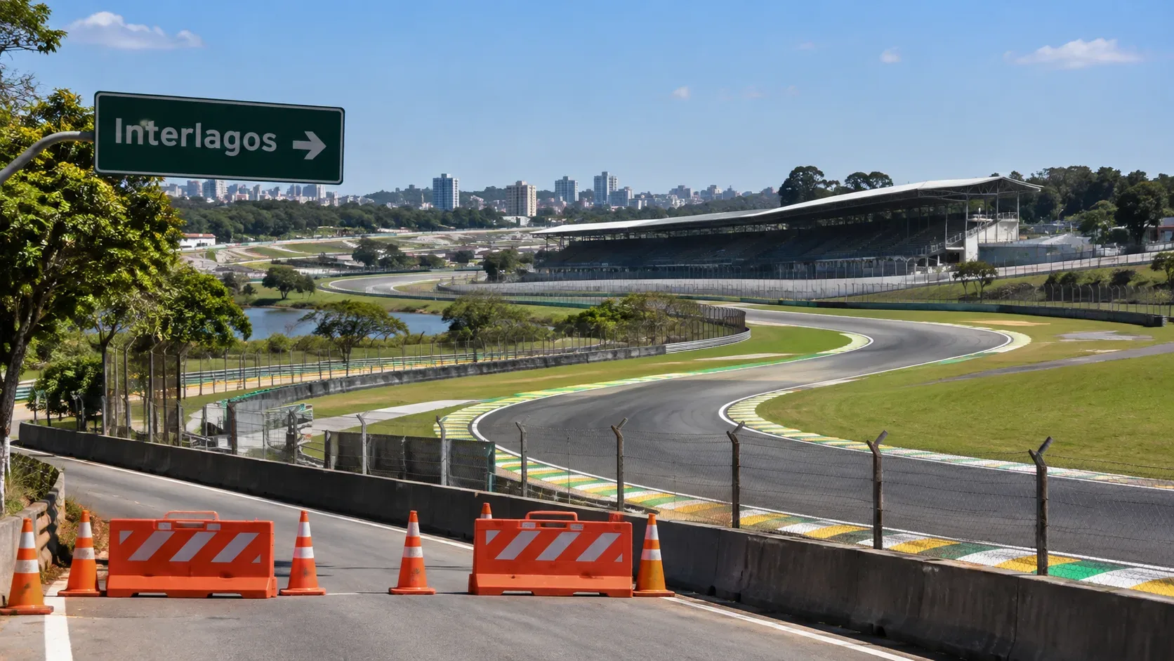 Vista ampla do Autódromo de Interlagos com pista, arquibancadas e uma via de acesso bloqueada por cones e barreiras, sob placa indicando Interlagos.